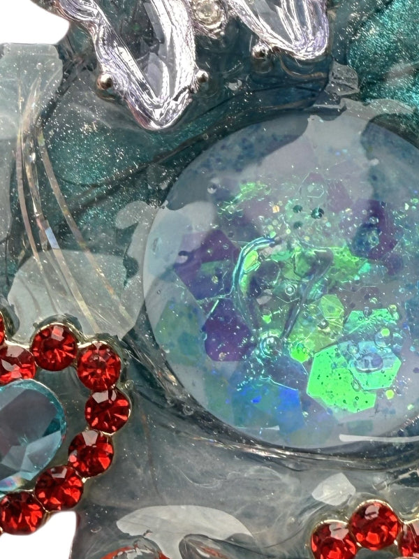 Close-up of a decorative dog charm with red gemstones and a colorful, iridescent center.