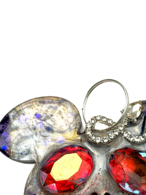 Close-up of a handcrafted dog collar tag charm with red gemstones and silver accents on a white background