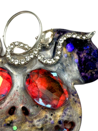 Close-up of a handcrafted dog collar tag charm with red gemstones and silver accents on a white background